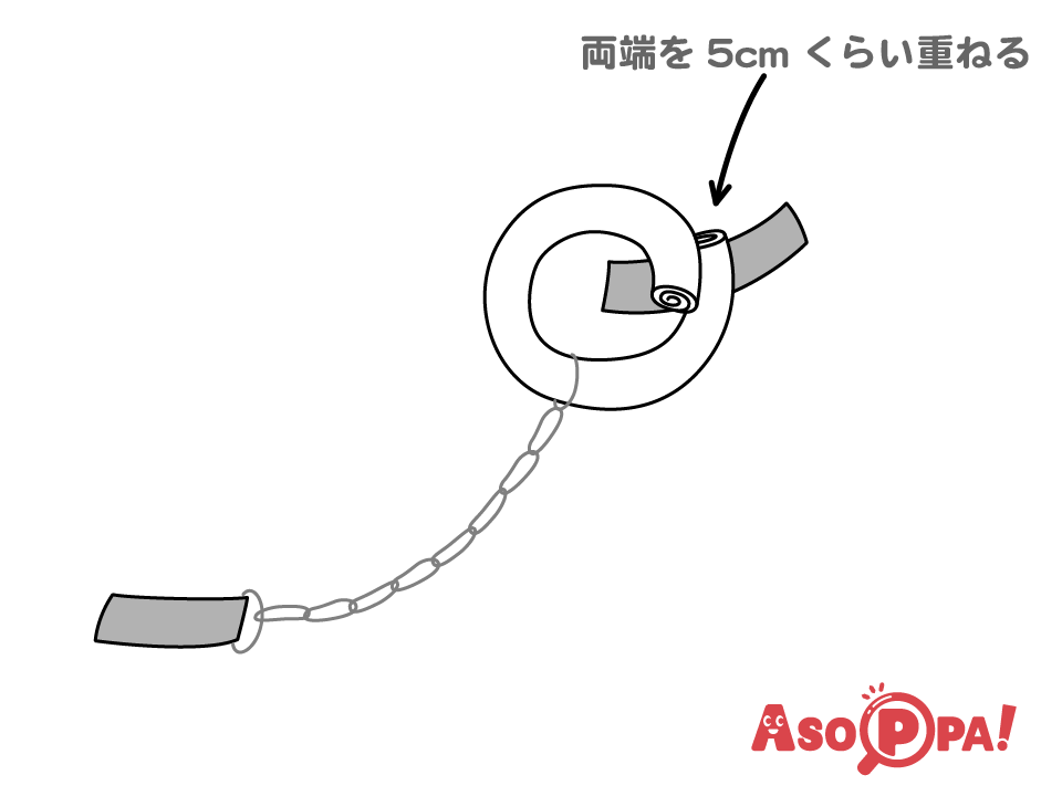 筒を輪にして両端を5ｃｍくらい重ね、ガムテープで固定する。輪ゴムのもう一方の端は床などに直接ガムテープで固定する。