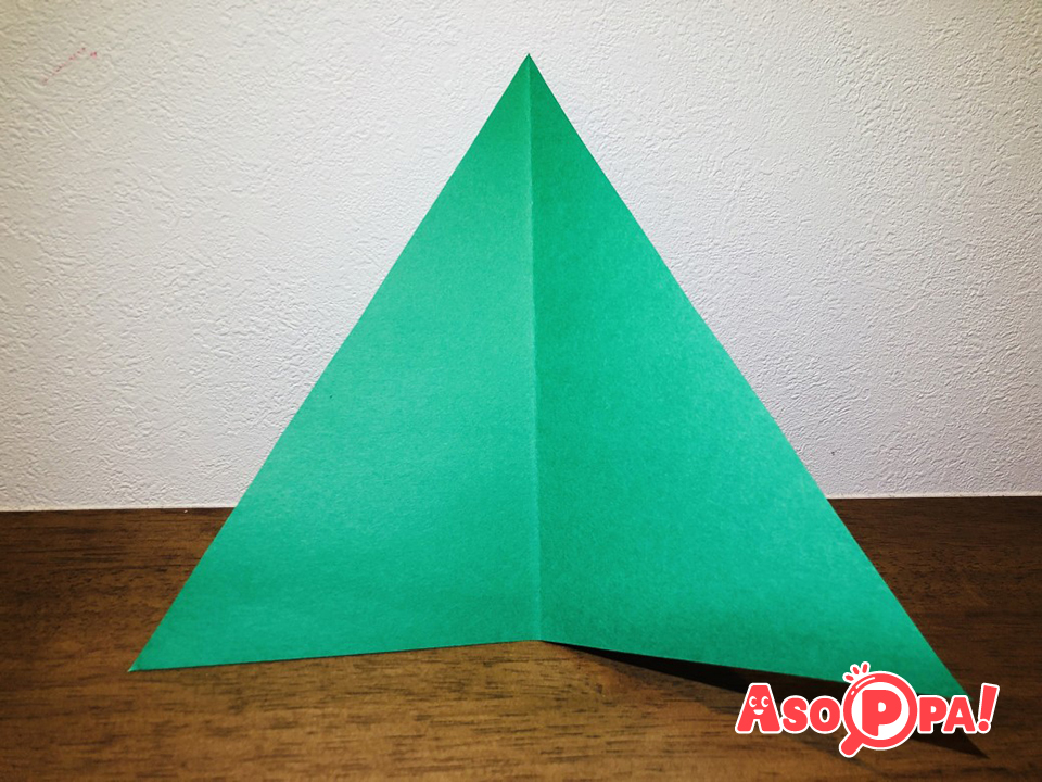 三角形に切った画用紙（緑）の真ん中に折りすじをつけます