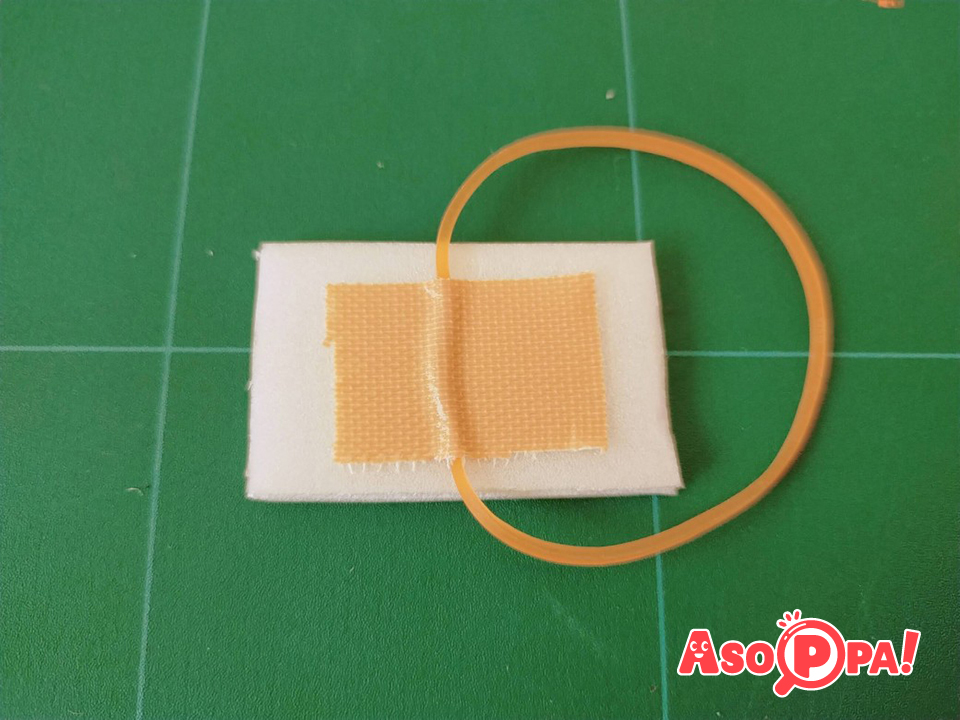 切り取った小さな四角に輪ゴムをかけ、ガムテープで真ん中に貼り付けます。