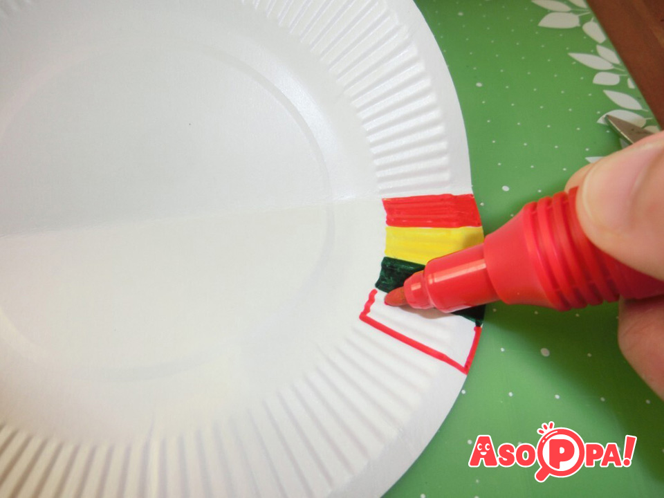 次に、ひな人形が座る台座を作ります。
紙皿を半分に折って垂直に立たせ、下の部分のギザギザしたところに色を付けます。
どんな色でもよいですが、赤・緑・黄などを使うとひなまつりの雰囲気が出ます。